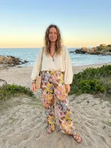 Pantalón palazzo de tiro alto con cintura elastizada, pierna ancha y estampado floral vibrante con predominancia de girasoles amarillos, flores rosadas y azules sobre fondo beige.