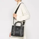 Cartera Guess modelo Jackie de color negro, confeccionada en PVC con textura saffiano. Cuenta con asas de mano fijas con tiras de tela estampada con la inscripción "GUESS LOS ANGELES", bolsillo frontal externo con el logotipo triangular metálico de la marca y correa ajustable para el hombro.
