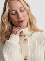 Cárdigan largo color crema, confeccionado en tejido de punto acanalado de viscosa. Tiene corte relajado, cierre frontal con botones y bolsillos de parche.