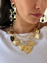 Collar dorado con cadena gruesa de eslabones y cadena fina de bolitas. Incluye varios dijes de corazones dorados con diferentes texturas y diseños, algunos con detalles en esmalte negro.