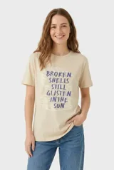 Remera de manga corta color beige, confeccionada en 100% algodón, con cuello redondo y estampa frontal con texto en tonos rosados.