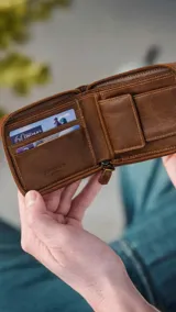 Billetera de cuero marrón oscuro con cierre perimetral. Presenta un detalle de doble pespunte artesanal en el frente y el logo grabado. El interior cuenta con compartimentos para billetes, tarjeteros y un monedero con broche.