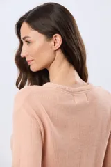 Buzo tejido liso de manga larga con cuello redondo, confeccionado en algodón de tejido grueso. Presenta bordes acanalados en el cuello, los puños y la cintura, con un pequeño detalle de placa metálica en el lateral inferior.