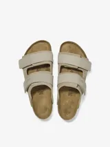 Sandalia Birkenstock modelo Uji en color taupe, confeccionada con una parte superior de gamuza suave y correas de nobuk con cierre de velcro. Presenta la clásica plantilla anatómica de corcho y suela de EVA.