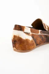 Mocasines de cuero con estampado animal print marrón y blanco, con suela marrón clara.