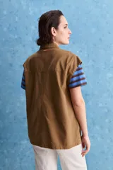 Chaleco de algodón color beige, de calce relajado, con cuello clásico, hombros amplios, cierre frontal con broches metálicos y bolsillos delanteros con solapa.