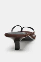 Sandalia tipo chinela de ante color marrón oscuro, con tacón kitten bajo y fino. Posee dos tiras finas en la parte delantera, una de ellas con separación para el dedo pulgar.