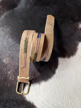 Cinto de cuero marrón claro con detalles bordados geométricos en tonos azul, rojo y beige, hebilla metálica de bronce y puntera forrada en cuero.