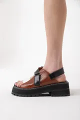 Sandalias de cuero color marrón con tiras cruzadas en blanco y negro, suela track y ajuste con velcro.