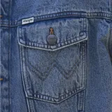 Campera de jean Wrangler en tono azul lavado, con cierre frontal de botones metálicos, cuello clásico y dos bolsillos frontales con solapa y detalle de costura en W.