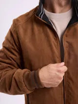 Campera reversible de gamuza sintética color marrón, con cierre frontal, cuello alto y puños de tejido acanalado con detalles de rayas.
