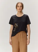 Remera negra de manga corta con cuello redondo y detalle de bordado floral en tono tostado en la parte inferior derecha.