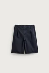 Bermuda de denim color azul marino, de corte relaxed fit con pliegues frontales, bolsillos laterales y cierre frontal con cremallera y botón.