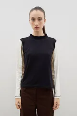 Remera de manga larga con cuello alto, diseño color block que combina un panel frontal y trasero negro con mangas en tonos blanco y beige, destacando costuras expuestas en contraste.