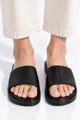 Sandalias planas de eco cuero color negro, con tira ancha superior y suela cómoda.