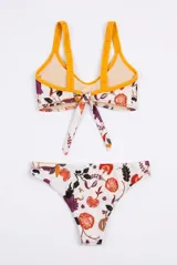 Conjunto de bikini de dos piezas con estampado floral en tonos rojo, violeta y verde sobre fondo claro, con detalles en color amarillo en los bordes y tirantes. El corpiño es de estilo deportivo con tiras para anudar al frente, y la bombacha es de corte clásico.