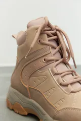 Zapatilla tipo hiking de caña media, confeccionada en una combinación de símil cuero y nylon en tonos beige y rosa suave. Presenta cordones al tono, interior acolchado para mayor abrigo y suela de goma dentada en color marrón con entresuela gris.