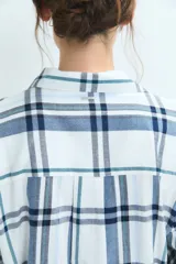 Pijama de dos piezas con estampado de cuadros en tonos azules y blancos. La parte superior es una camisa de manga larga con cuello camisero y cierre frontal de botones. La parte inferior es un pantalón de corte recto con cintura elástica.