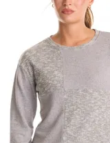 Buzo de manga larga con cuello a la base, confeccionado en tejidos combinados con texturas lisas y acanaladas. Presenta un diseño con tajos laterales en el ruedo.