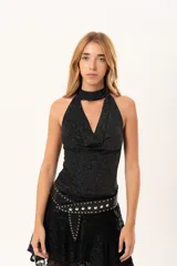 Top sin mangas de tejido lurex negro con acabado brillante, cuello halter y escote cruzado.