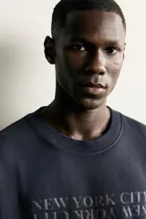 Camiseta de corte relajado con cuello redondo y manga corta. Presenta un diseño con bordados y estampados combinados a contraste en el frente con la inscripción 'New York City' y un efecto de lavado en la tela.