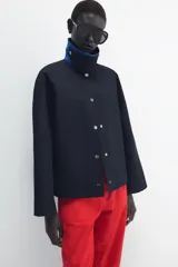 Chaqueta de Zara Woman Collection color negro, de cuello con solapa y manga larga. Cuenta con bolsillos delanteros ocultos en las costuras, cierre frontal con botones metálicos a presión y detalle de diseño asimétrico en azul en el cuello.
