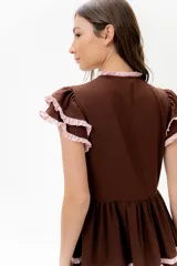 Vestido midi de lino blanco con diseño de broderie, cuello alto, cierre frontal con botones y volados decorativos en los hombros y el cuerpo.