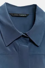 Camisa azul de manga corta y cuello solapa con costura horizontal en el pecho y cierre frontal oculto con botones.
