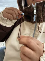 Campera de gabardina con diseño bicolor en tonos crudo y chocolate, con capucha forrada en polar. Presenta cierre frontal, mangas largas con puños elásticos y un parche distintivo en la manga.