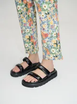 Sandalias de cuero vacuno color marrón con acabado brillante, diseño de dos tiras anchas acolchadas y plataforma baja.
