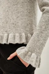Sweater de punto color gris melange, con cuello redondo, manga larga y detalle de volado en el ruedo. Presenta pequeñas aplicaciones de strass distribuidas por toda la prenda.