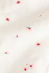 Braga de bikini cheeky de talle medio, color crudo con delicado estampado de pequeñas flores rojas y verdes, y ribete con terminación en ondas.