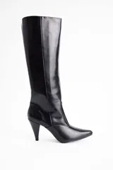 Bota de caña alta confeccionada en cuero vegano color negro, con punta fina y taco cónico de altura media.