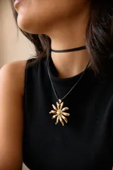 Collar con dije de acero quirúrgico en forma de flor tipo margarita, montado sobre un tiento de cuero negro.