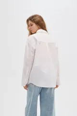 Camisa de algodón blanca, de corte oversize, manga larga y cuello camisero, decorada con apliques de strass y bordados sutiles en la parte delantera.