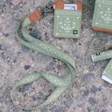 Llavero para cuello color verde con diseño estampado geométrico y floral en tono claro. Cuenta con un aplique de cuero sintético marrón con detalle grabado y un gancho mosquetón metálico oscurecido.