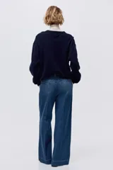 Pantalón de jean de tiro alto con corte wide leg y piernas amplias. Presenta diseño con raya frontal marcada, cierre con botón oculto, bolsillos laterales al bies y bolsillos traseros decorativos.