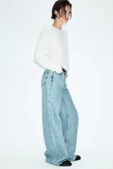 Jeans de tiro alto con diseño wide leg y cinco bolsillos. Presenta cierre frontal con cremallera y botón, e incluye un cinturón a contraste con hebilla metálica.