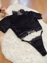 Conjunto de lencería compuesto por un top de cuello alto y una tanga, confeccionados en terciopelo negro con detalles de encaje y microtul. El top presenta mangas cortas con terminaciones en encaje y el borde inferior decorado con una cinta y encaje. La tanga es regulable y combina la textura del terciopelo con bordes de encaje.