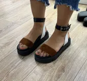 Sandalias negras de plataforma gruesa con tira ancha de charol brillante sobre los dedos y tira de gamuza ajustable con hebilla metálica en el tobillo.