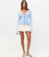 Saco de tricot celeste con textura acanalada vertical, escote en V y cierre frontal con lazos atables. Presenta mangas largas con puños acampanados con volados, al igual que el ruedo.