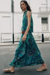 Top sin mangas de cuello alto con lazo ajustable, escote en V y diseño cruzado en el delantero. Presenta un estampado paisley en tonos verdes, azules y rosados, con bajo elástico y forro interior.