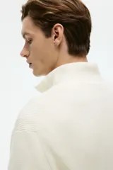 Buzo de punto color crema, con cuello alto y medio cierre metálico. Presenta un tejido acanalado en el cuello y un calce regular.