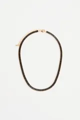 Collar tipo gargantilla con cristales negros rectangulares engarzados en metal dorado. Cuenta con cadena de extensión y cierre de mosquetón.