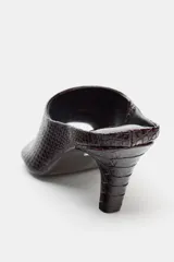 Sandalia tipo mule de tacón alto, color marrón oscuro con textura de piel de cocodrilo. Presenta punta cuadrada y un diseño abierto en la parte delantera.
