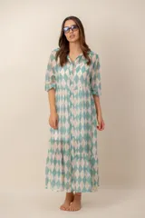 Vestido midi turquesa y blanco con estampado de rombos, cuello camisero, cierre frontal con botones y mangas cortas abullonadas. Cuenta con recortes fruncidos en la falda.