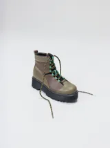 Botas de cuero estilo trekking, en combinación de colores verde, marrón y gris, con plataforma de goma negra, cordones bicolor inspirados en cuerdas de escalada y pasadores en tono rojizo.