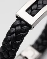 Pulsera de diseño masculino compuesta por una banda de cuerina trenzada en color negro y una placa central rectangular de acero inoxidable con acabado pulido.