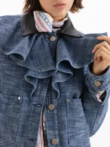 Chaqueta de denim Panamá azul de 100% algodón, con volados en el frente y cuello de cuero vacuno negro contrastante. Cuenta con bolsillos frontales con solapa y cierre de botones metálicos.