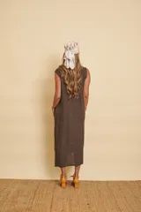 Vestido midi de lino color marrón, sin mangas y con escote en V. Presenta detalles de flecos a lo largo de la abertura y una franja bordada con lentejuelas en el ruedo. Incluye bolsillos laterales.